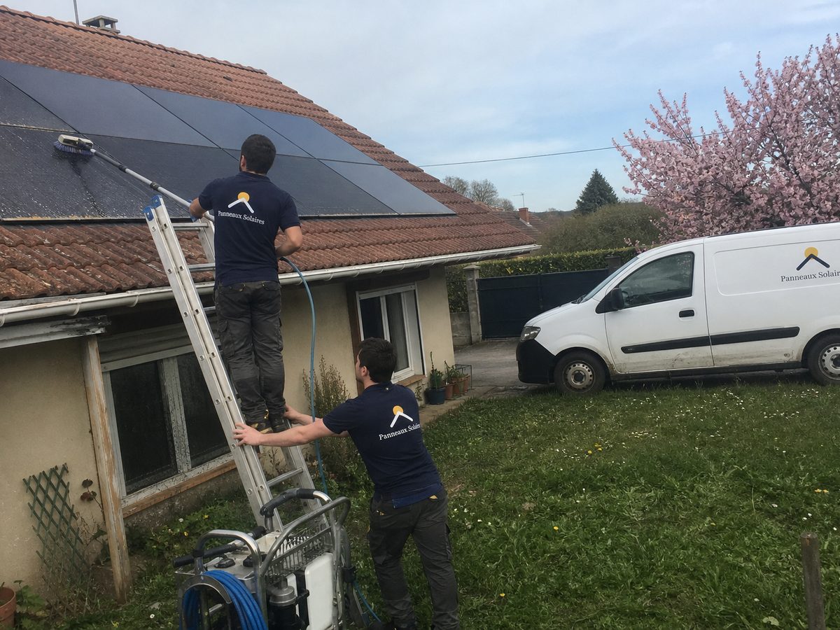 Un technicien nettoie les panneaux à la perche et à l'eau pure, le pollen encore visible au bas des panneaux