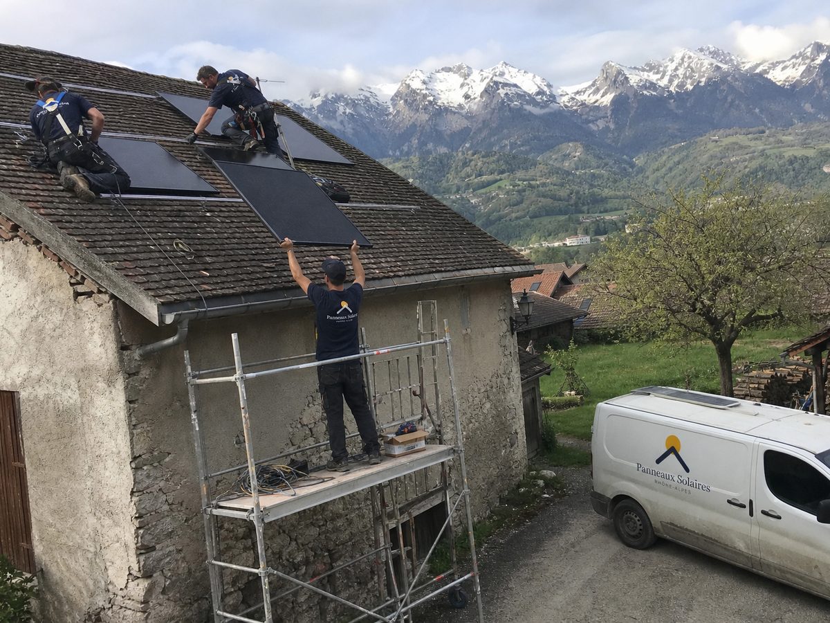 Pose de panneaux sur une ferme de vallée, montagnes enneigées derrière