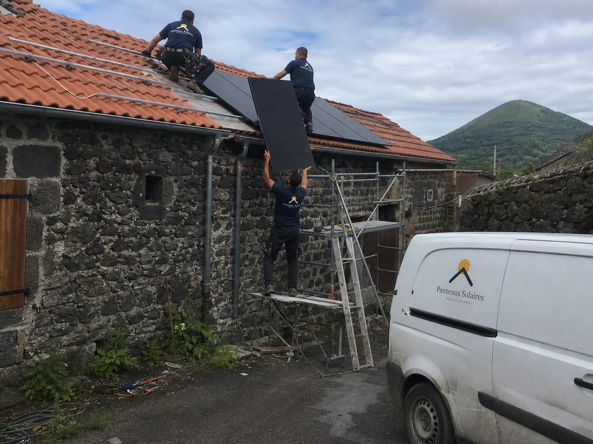 Pose de panneaux sur une maison en pierre volcanique, un volcan derrière