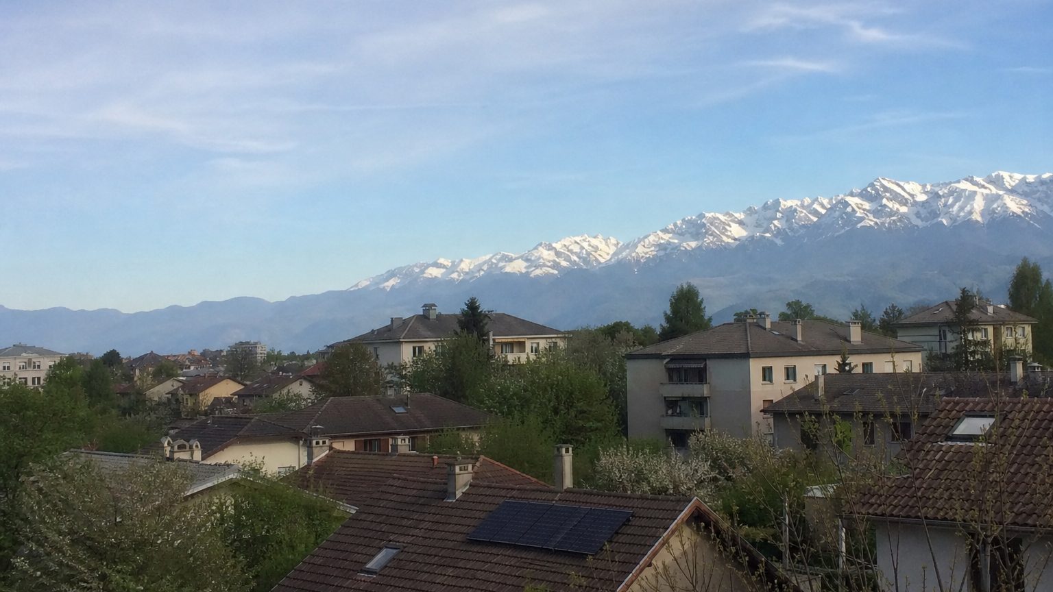 Toits d'un quartier résidentiel, plusieurs équipés de panneaux, montagnes enneigées au fond
