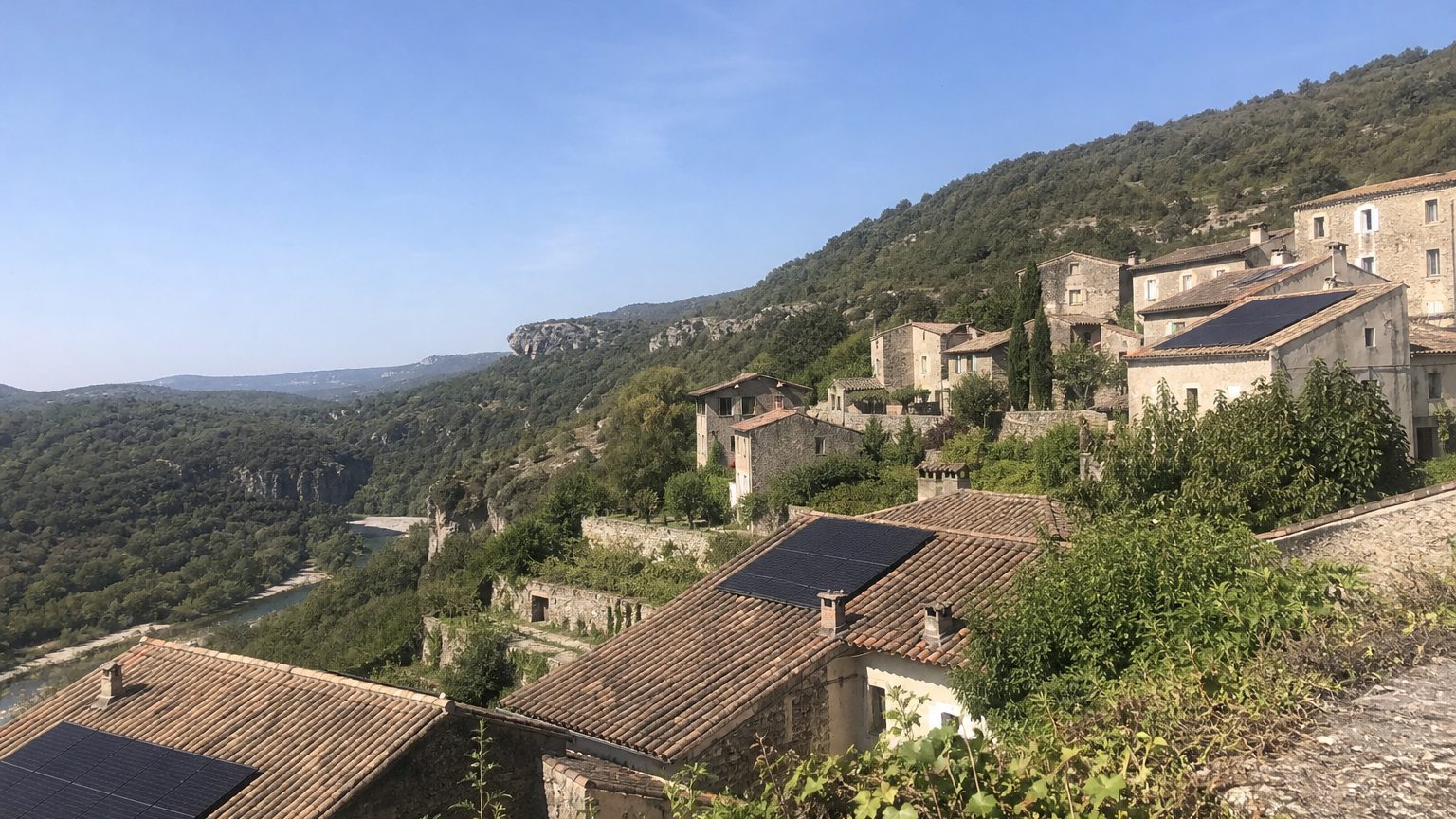 Village de pierre calcaire à flanc de vallée, toits en tuile canal, quelques panneaux