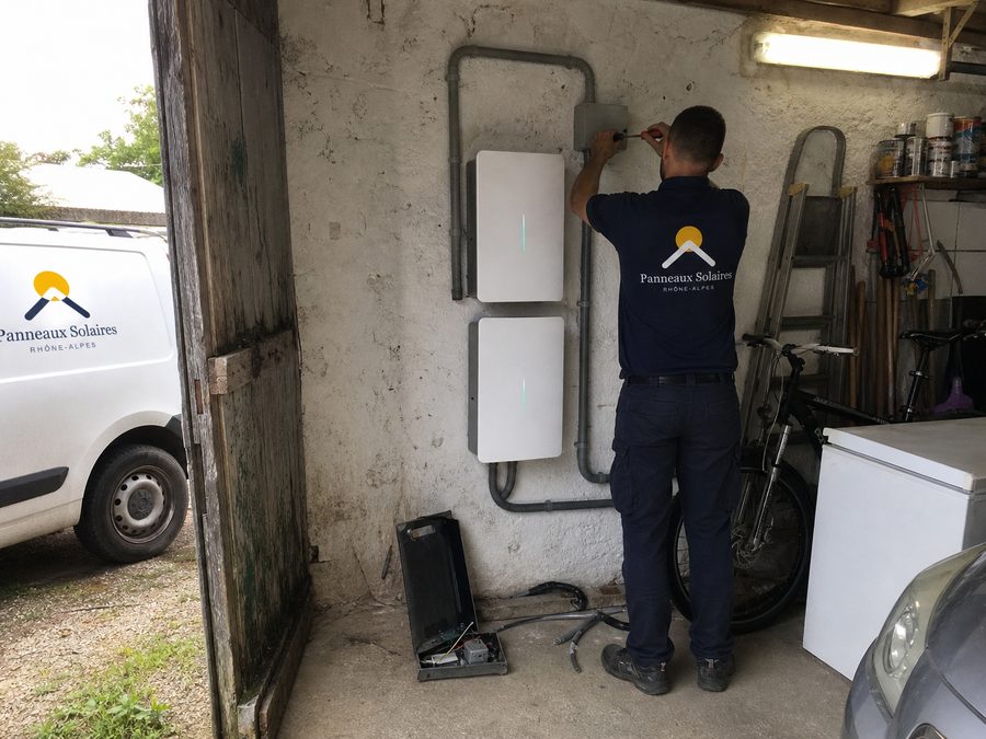 Les deux batteries au mur du garage, un technicien serre les presse-étoupes, vélos et congélateur autour