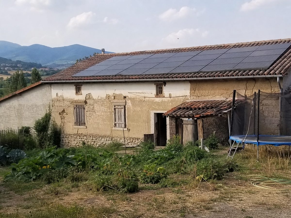 Ferme en pisé à Montbrison, vingt panneaux sur le toit en tuile canal, les monts du Forez à l'horizon