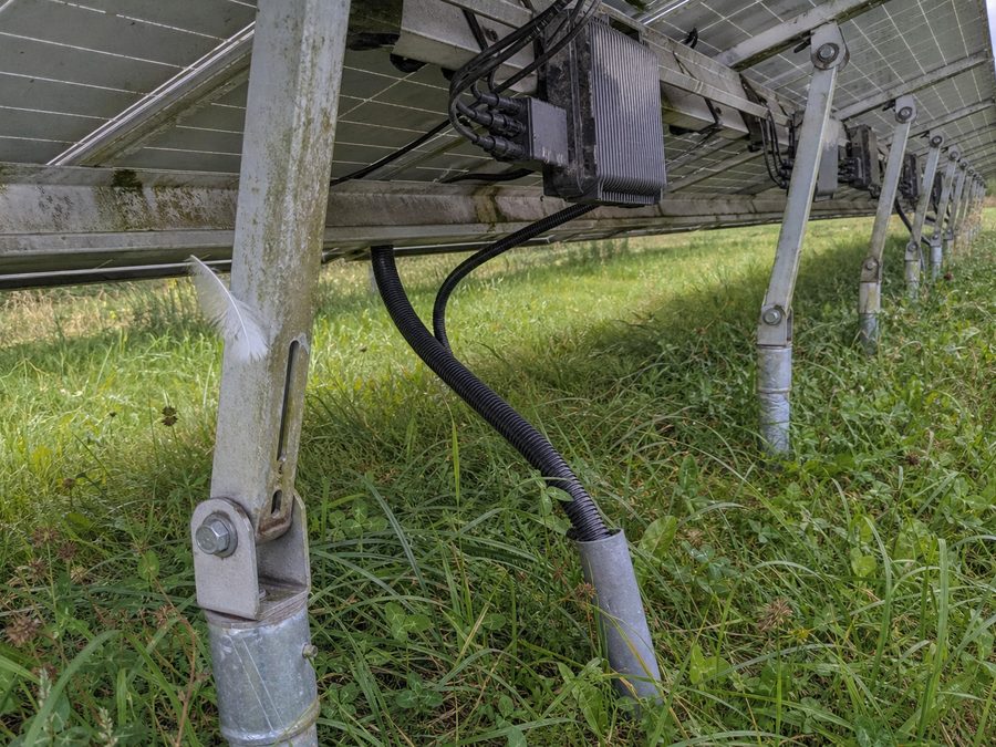 L'arrière du châssis : pieds en aluminium sur pieux vissés, micro-onduleurs sous les panneaux, herbe haute