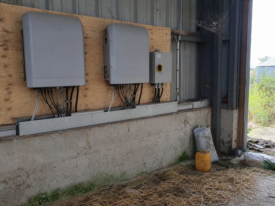 Les deux onduleurs sur leur panneau de bois, dans un coin du hangar, avec la paille au sol