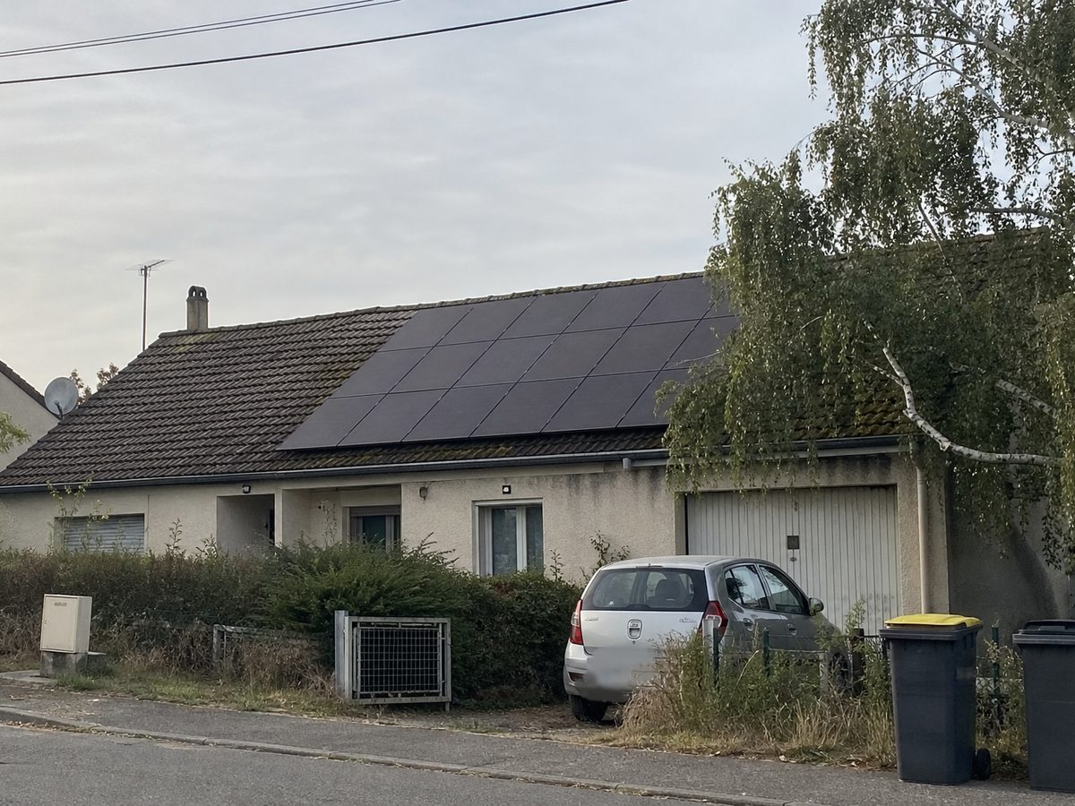 Maison de lotissement à Villefontaine, quinze panneaux noirs sur le rampant en tuiles mécaniques, le bouleau du voisin au bas du toit