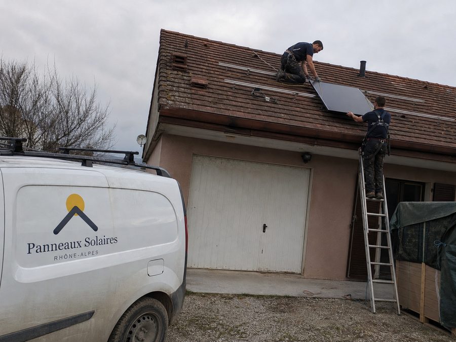 Deux techniciens posent les panneaux sur le rampant en tuiles mécaniques un matin de février, le camion dans l'allée