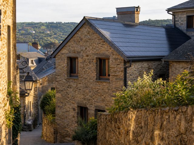 Rue d'un centre-bourg, toits en tuiles mécaniques dont l'un porte des tuiles solaires sans rupture de teinte